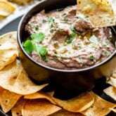 black bowl of hummus with a tortilla chip dunking in