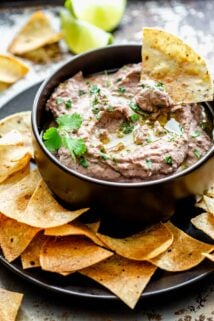 black bowl of hummus with a tortilla chip dunking in