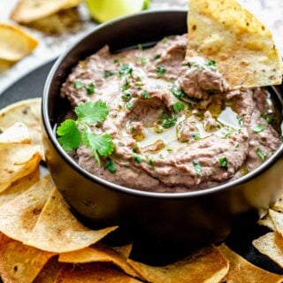black bowl of hummus with a tortilla chip dunking in