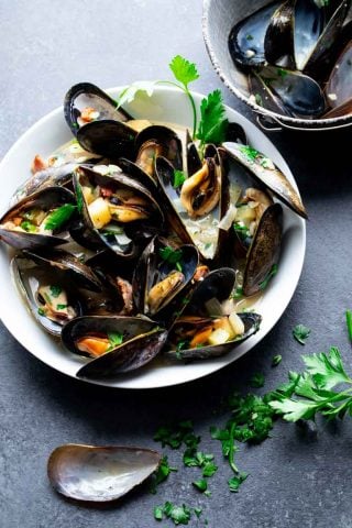 A black table with a white bowl with mussels