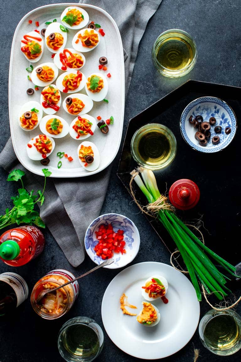 A black and gray surface with a platter of spicy deviled eggs on it and two glasses of wine