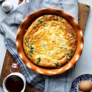 Spinach Egg Bake in a pie plate on a white table with a cutting board and blue kitchen towel