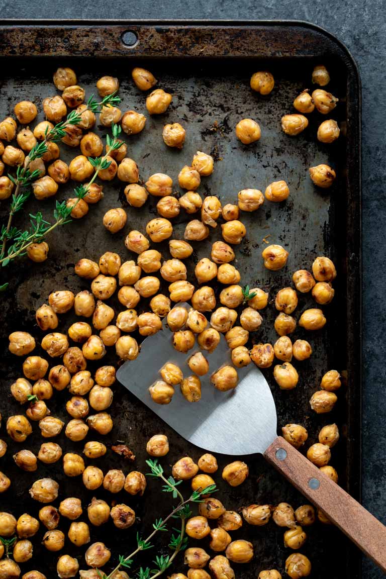 crispy roasted chickpeas and fresh thyme on a baking sheet with a spatula