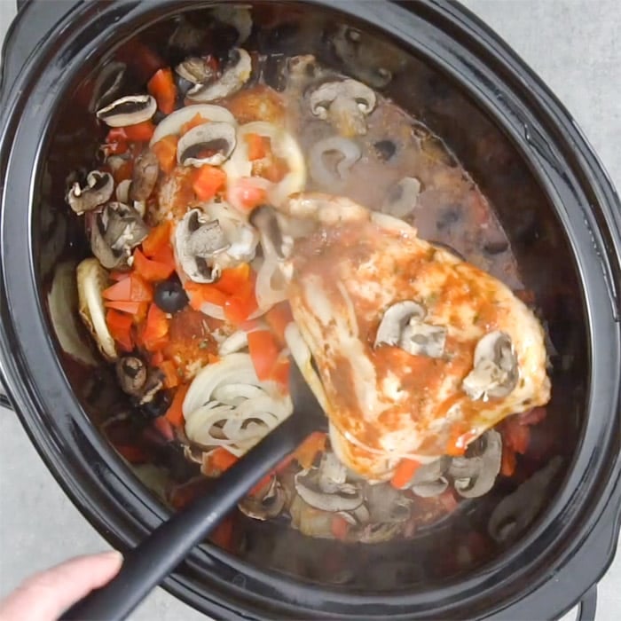 lifting a piece of chicken out of the slow cooker
