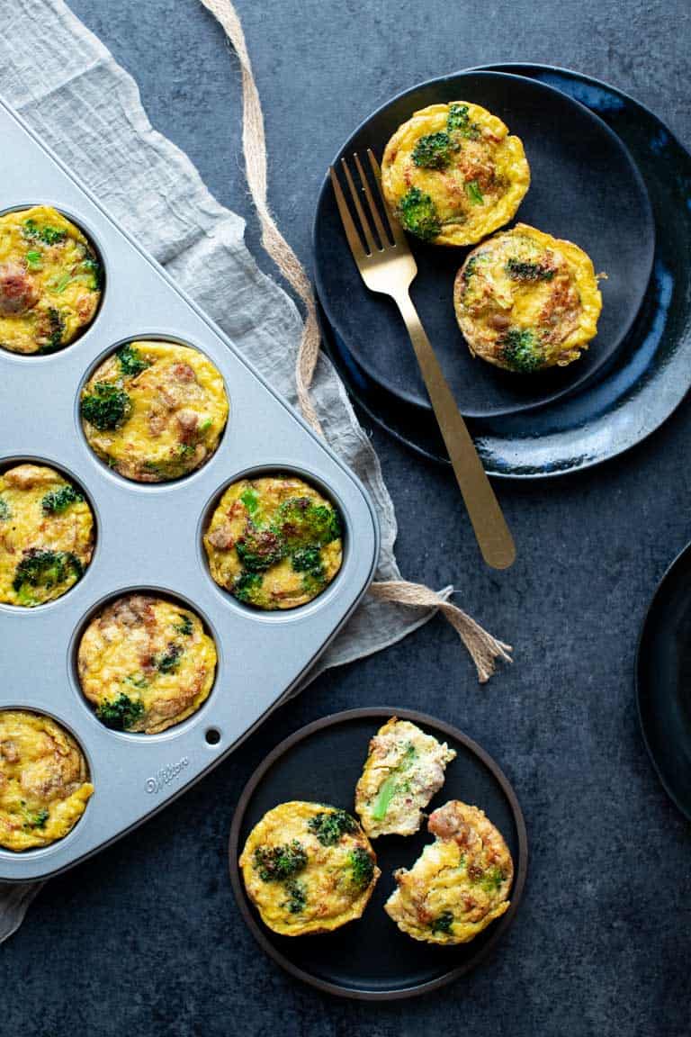 Overhead view of a charcoal gray table with a muffin tin, and two plates of paleo egg muffins