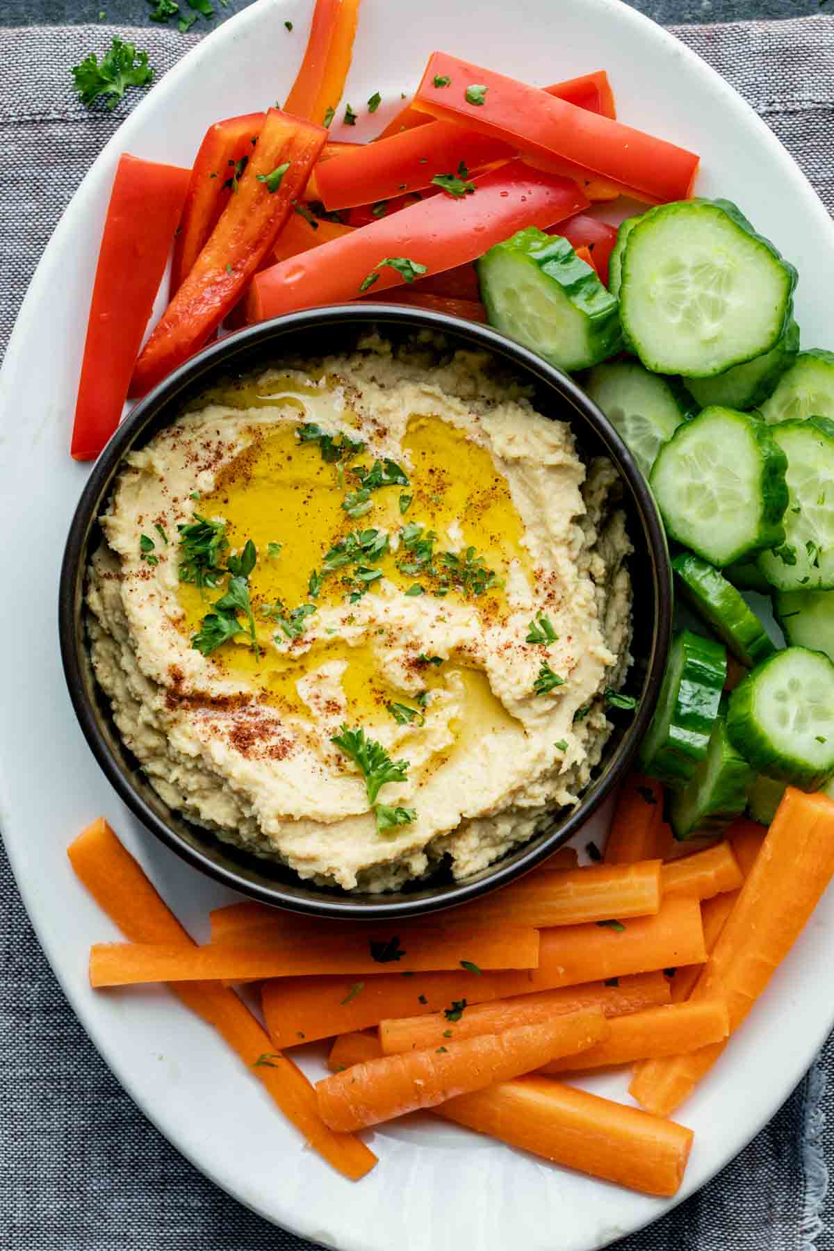 a white oval platter with the bowl of hummus and veggies on it