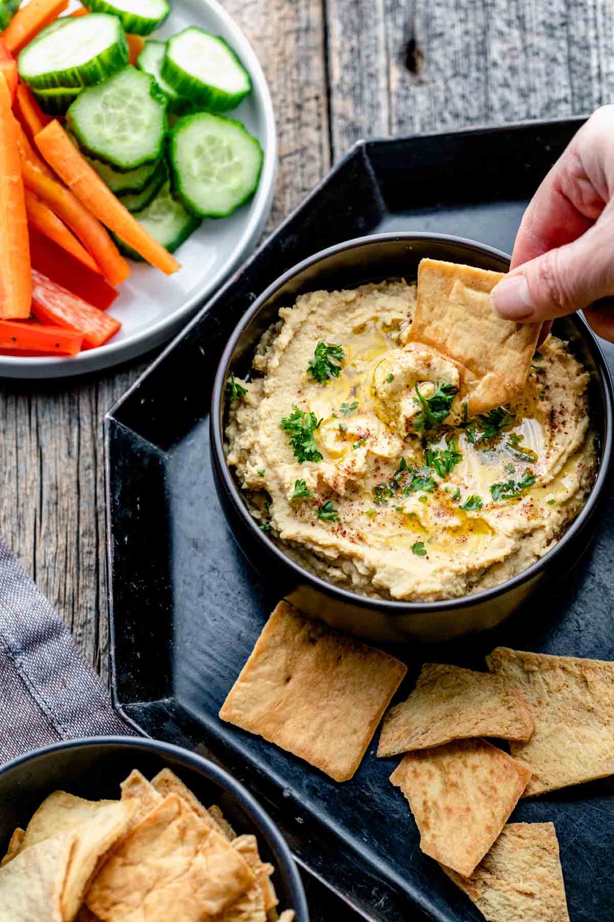 the bowl of hummus on a black tray with a pita chip being dipped into it
