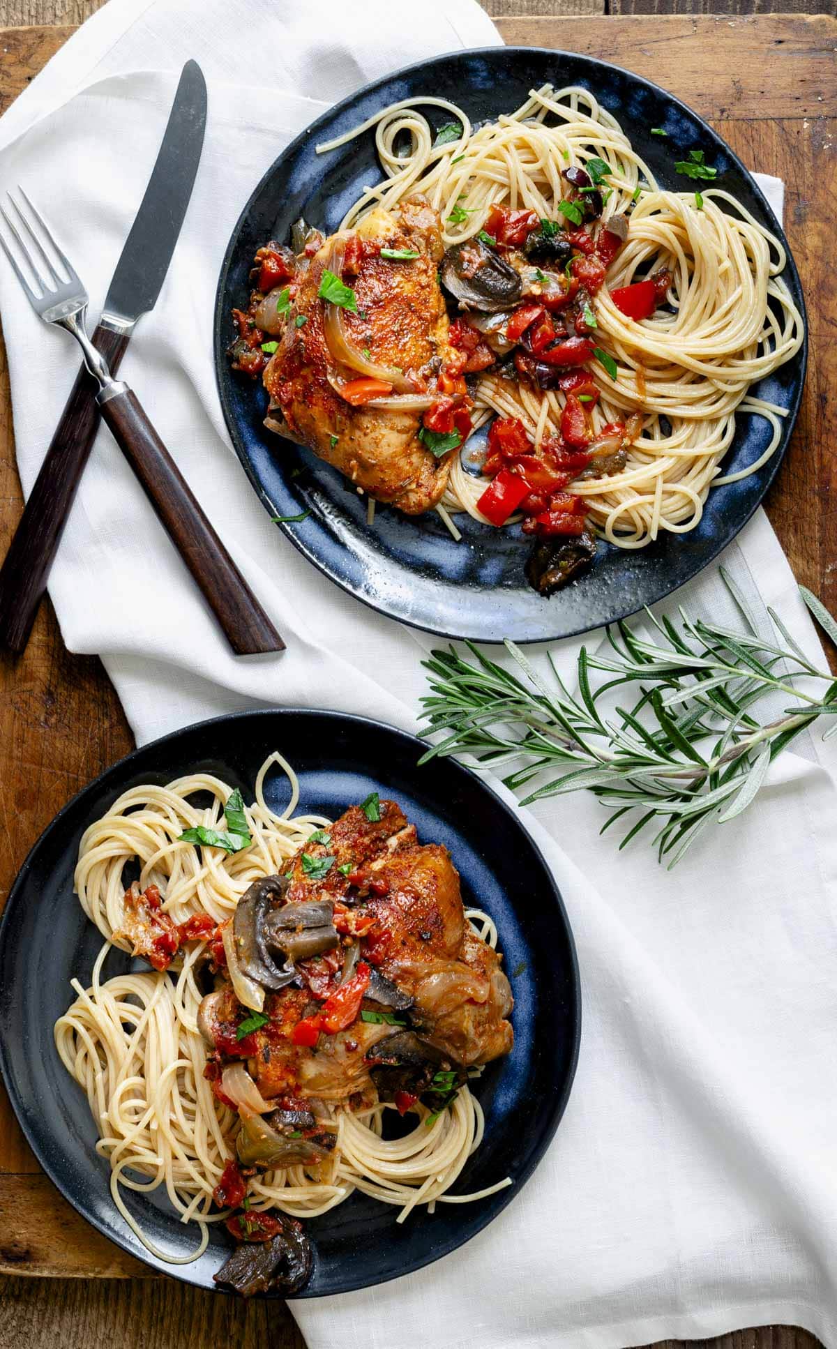 two blue plates of chicken cacciatore on pasta