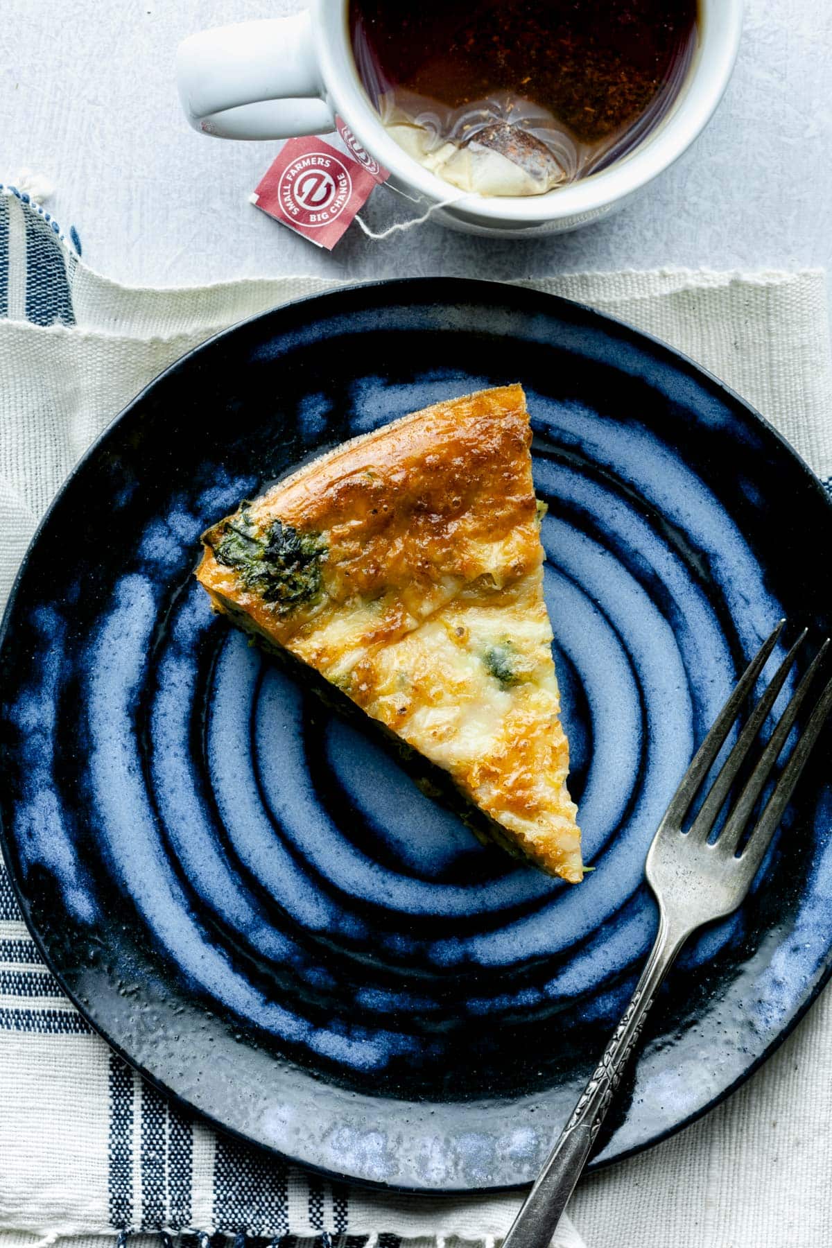 a slice of the egg bake on a blue plate with a cup of tea at the top of the frame