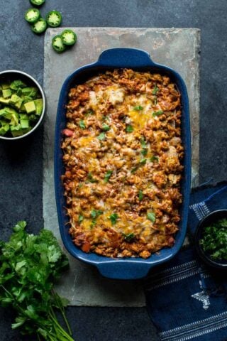 Layered Chicken Enchilada Casserole in a baking dish with cilantro and avocado