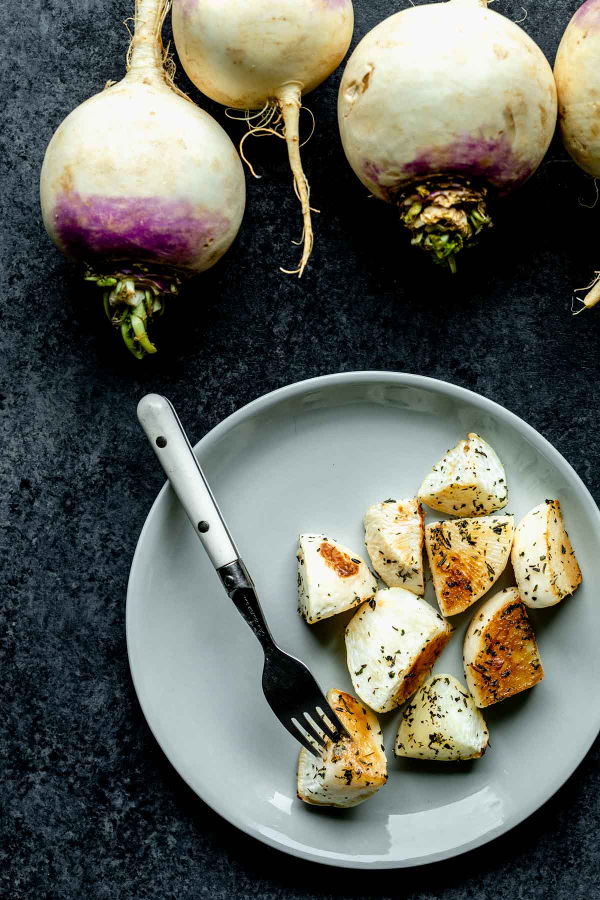 a plate of turnips with unpeeled purple top turnips on the tabletop too