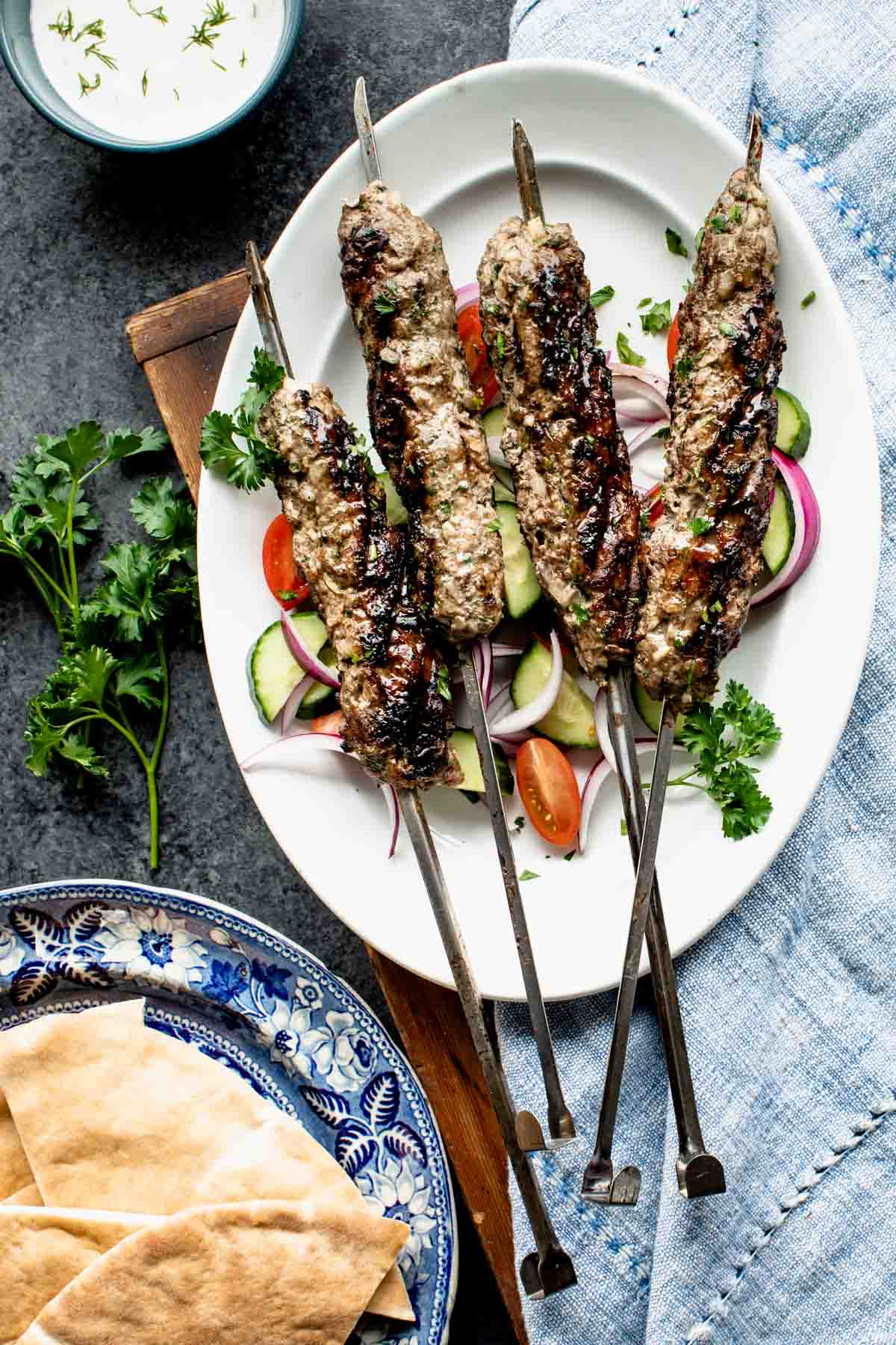 overhead of table with yogurt sauce, pitas and lamb kofta with blue napkin