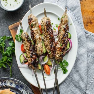 overhead of table with yogurt sauce, pitas and lamb kofta with blue napkin