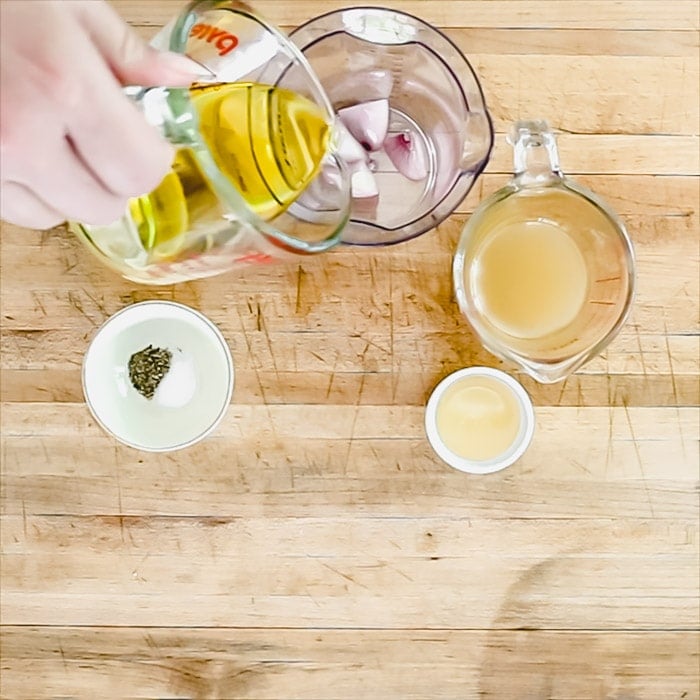 pouring olive oil into a blending jar with shallot