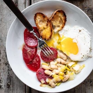 a white bowl with grilled baguette, poached eggs, white beans and sliced beets