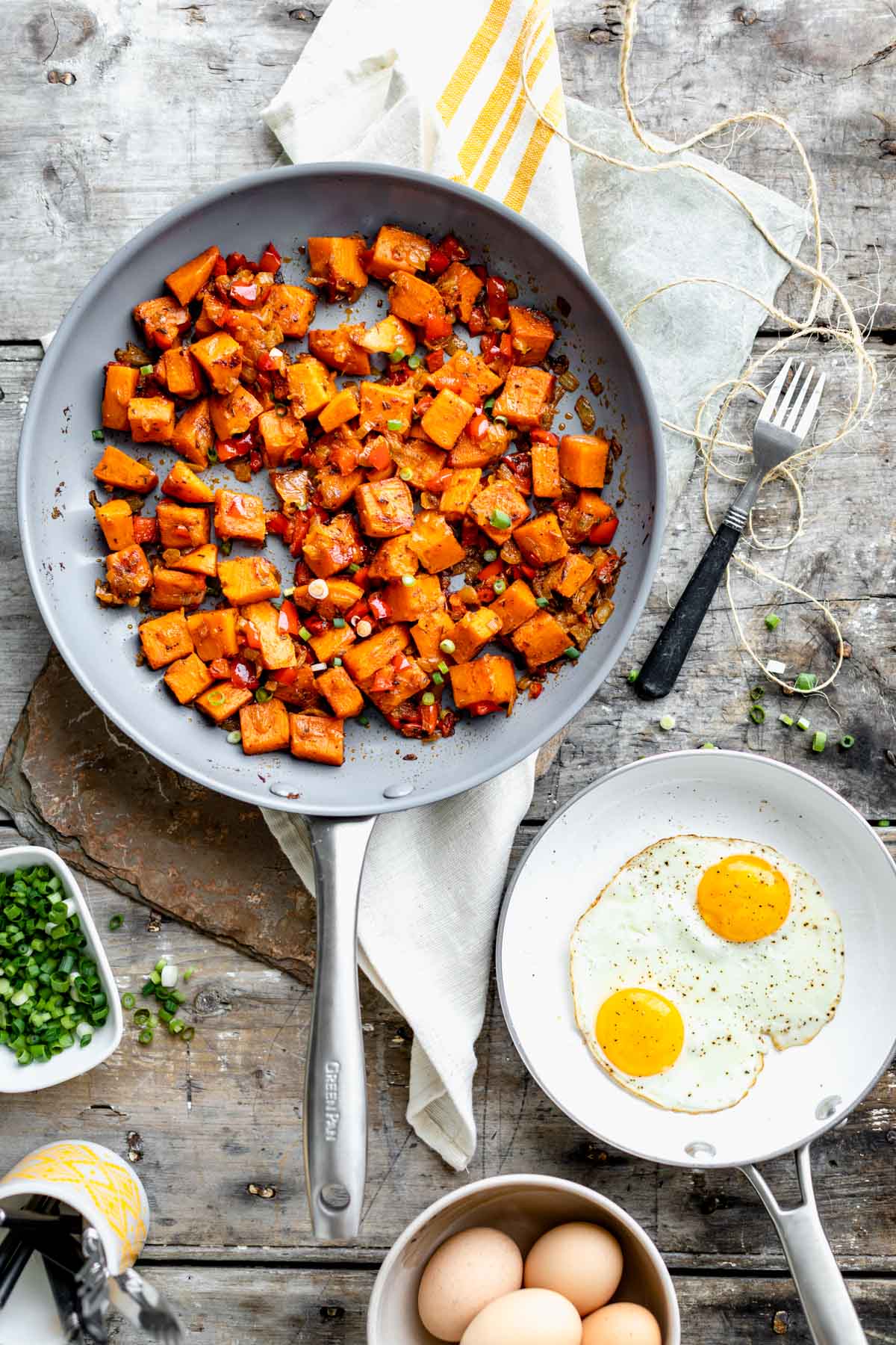 a skillet of hash from overhead with a skillet of eggs on a gray wooden table top