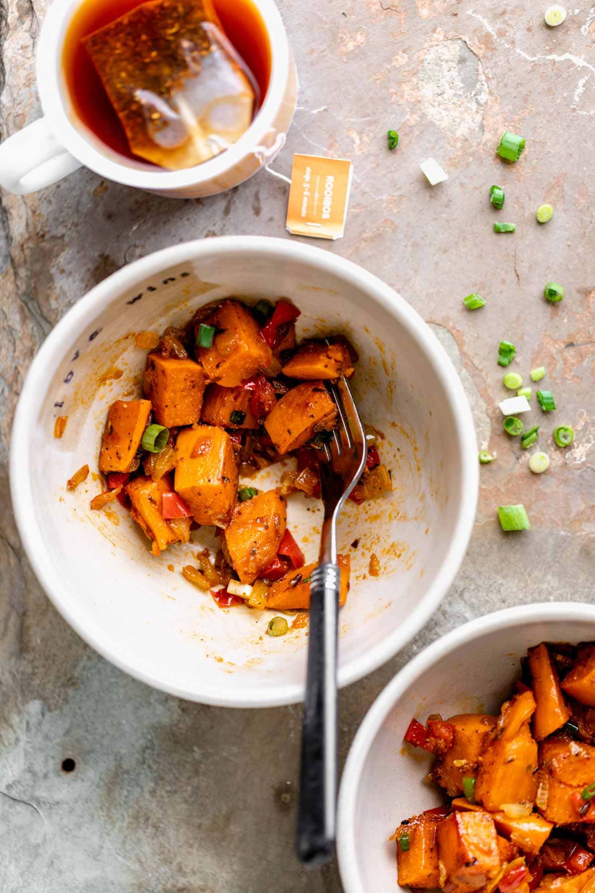 overhead of bowl of hash being eaten with a fork and a cup of tea