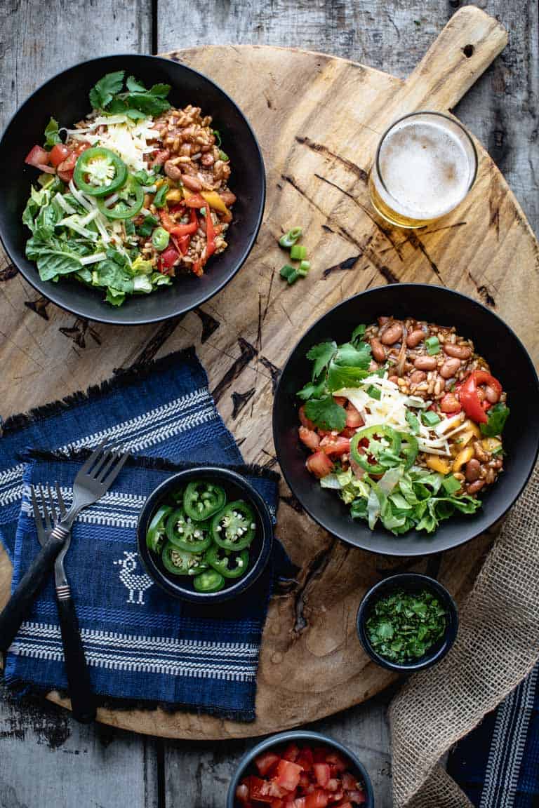 2 vegetarian burrito bowls on a wooden board surrounded by topping ingredients