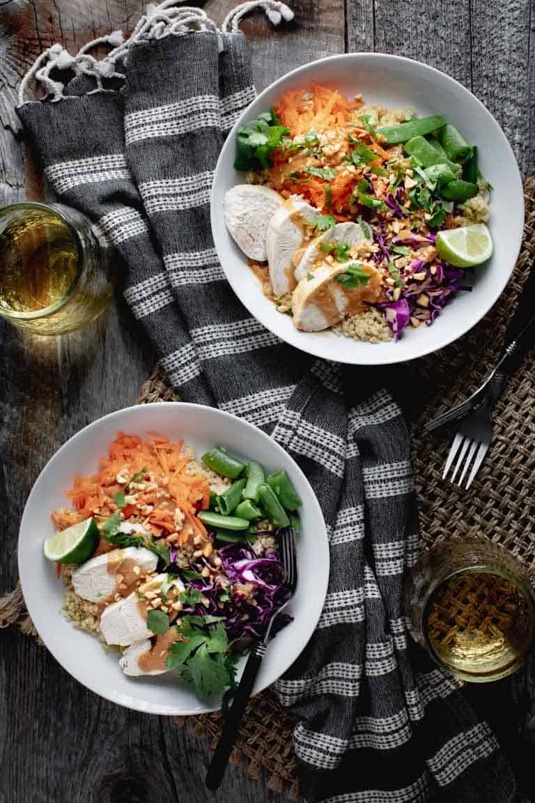 An overhead view of a farm table with two buddha bowls with quinoa and chicken