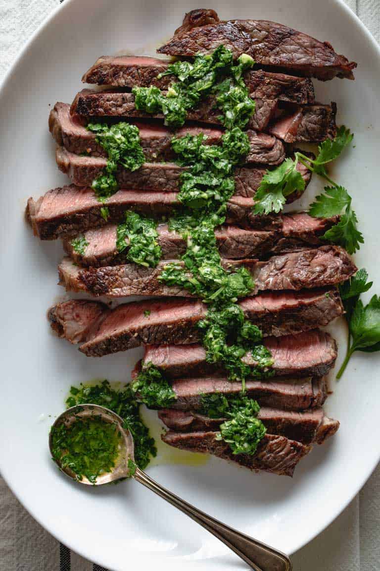 A close up view of sliced grilled sirloin steak with green chimichurri sauce on it