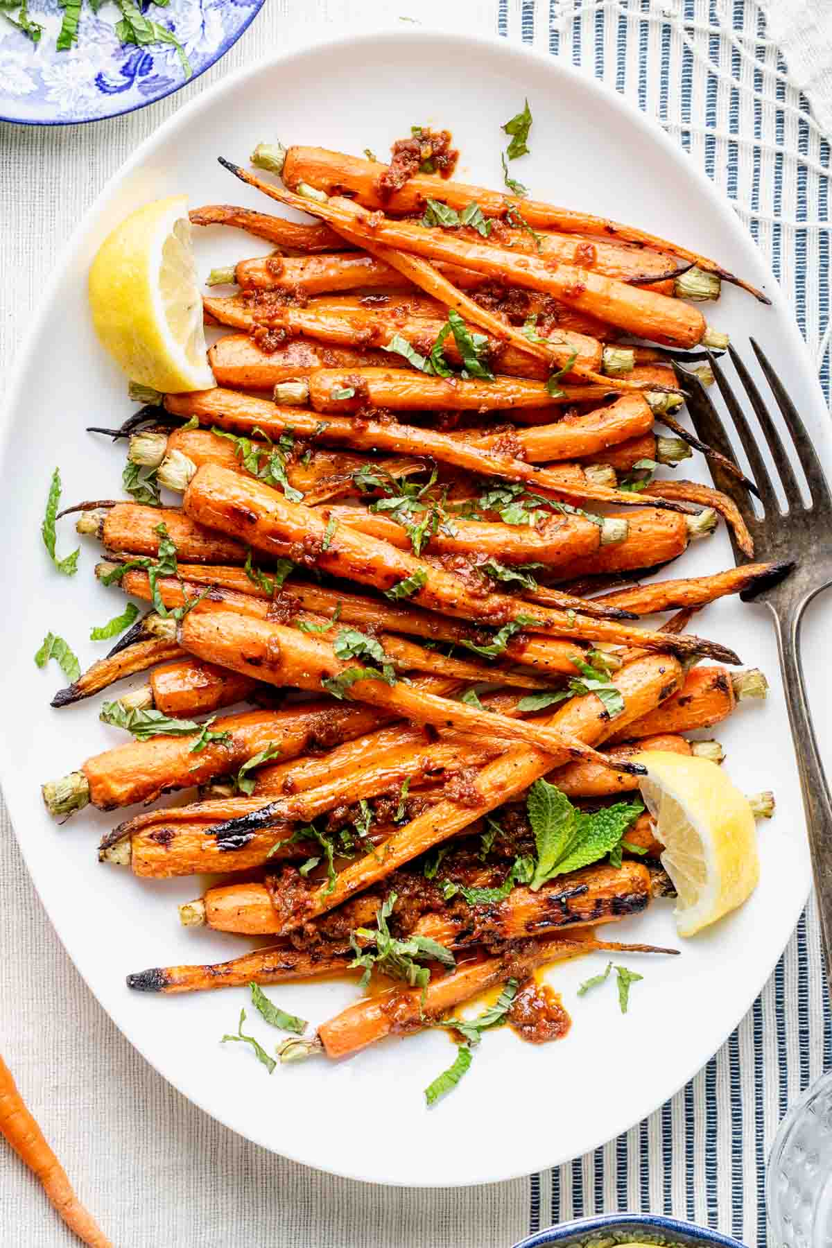 the grilled carrots with lemon and harissa on a white platter with a serving fork