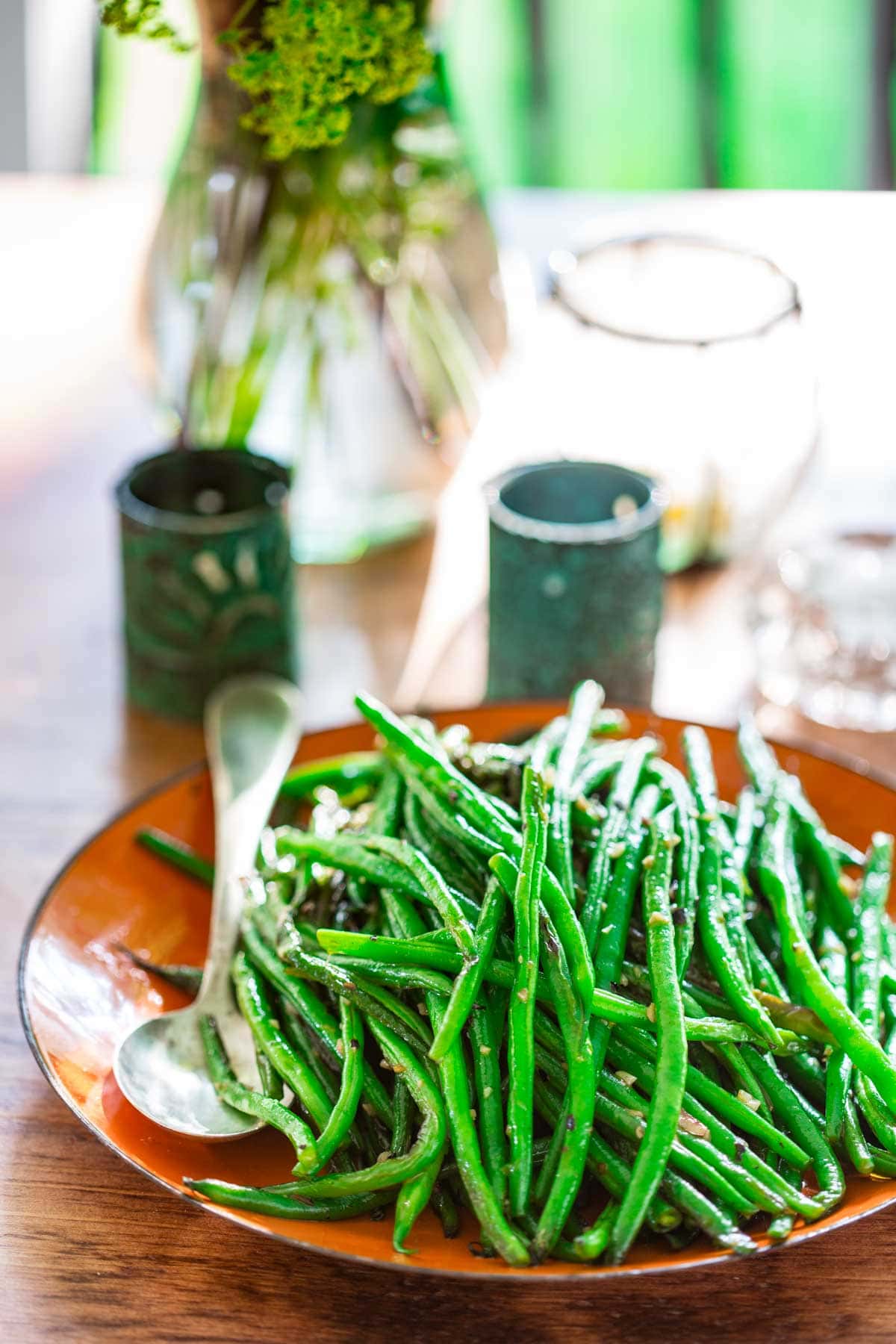 a table with votive candles, flowers and an orange platter piled with cooked green beans