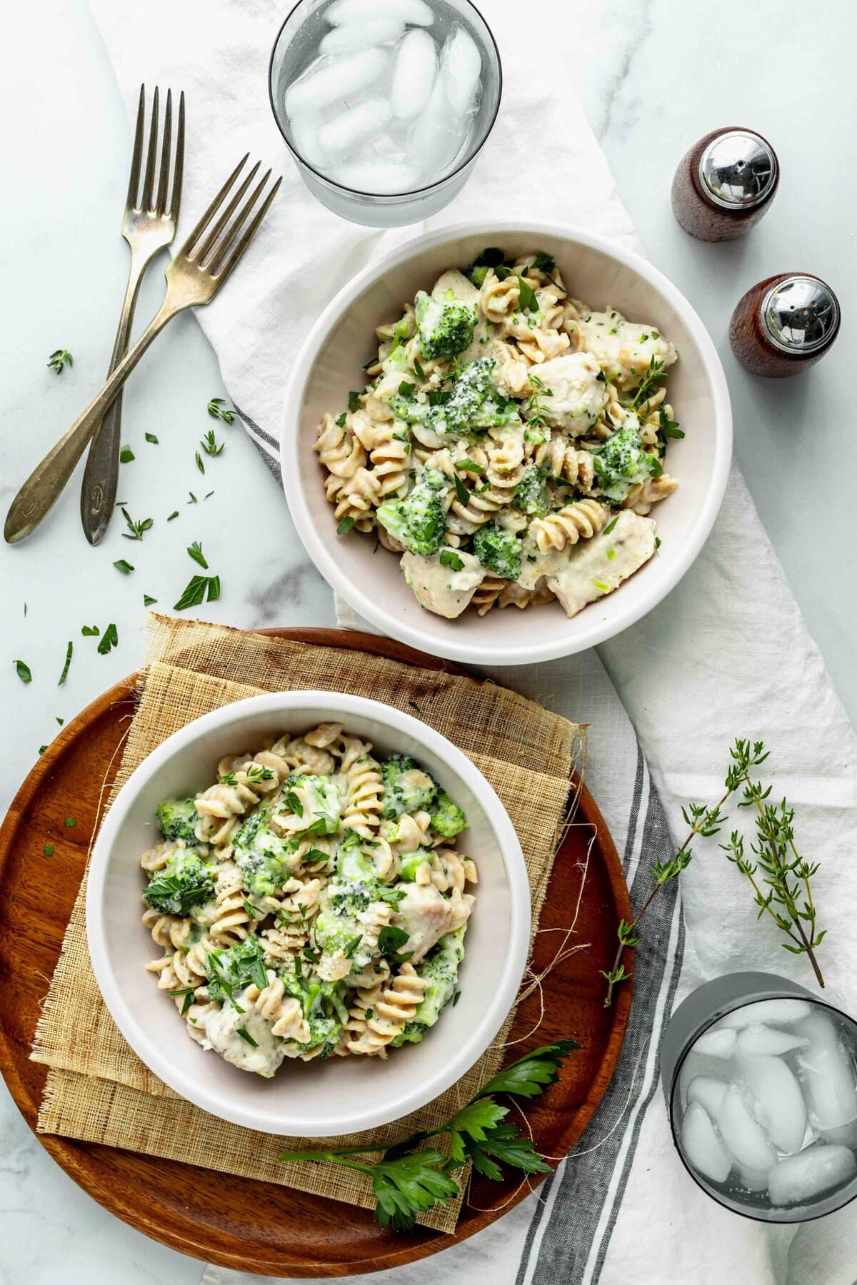 A marble counter with two bowls of chicken alfredo with broccoli plus two glasses of ice water