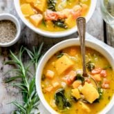 two white bowls of veggie soup with rosemary sprig and a white napkin