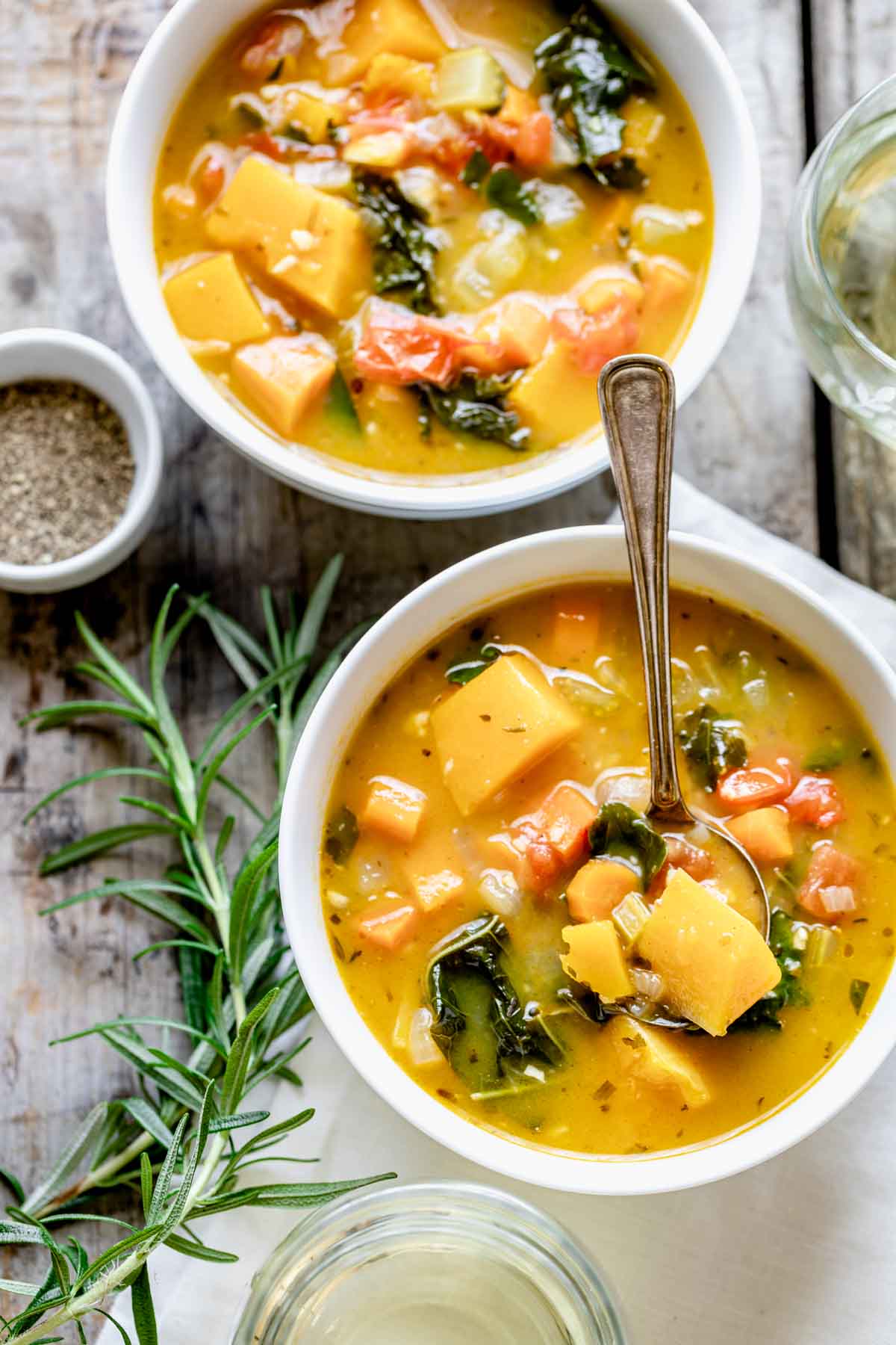 two white bowls of veggie soup with rosemary sprig and a white napkin