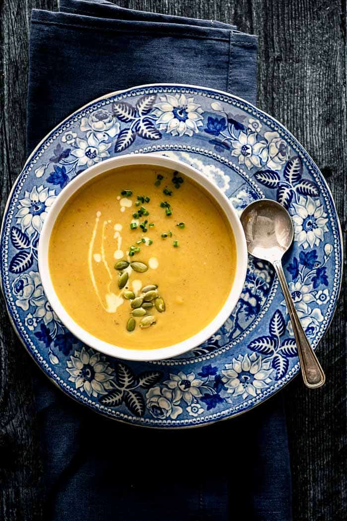 A blue and white patterned plate underneath a white bowl of pumpkin soup