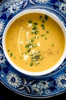 A blue and white patterned plate underneath a white bowl of pumpkin soup