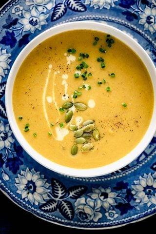 A blue and white patterned plate underneath a white bowl of pumpkin soup
