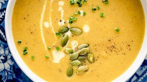 A blue and white patterned plate underneath a white bowl of pumpkin soup
