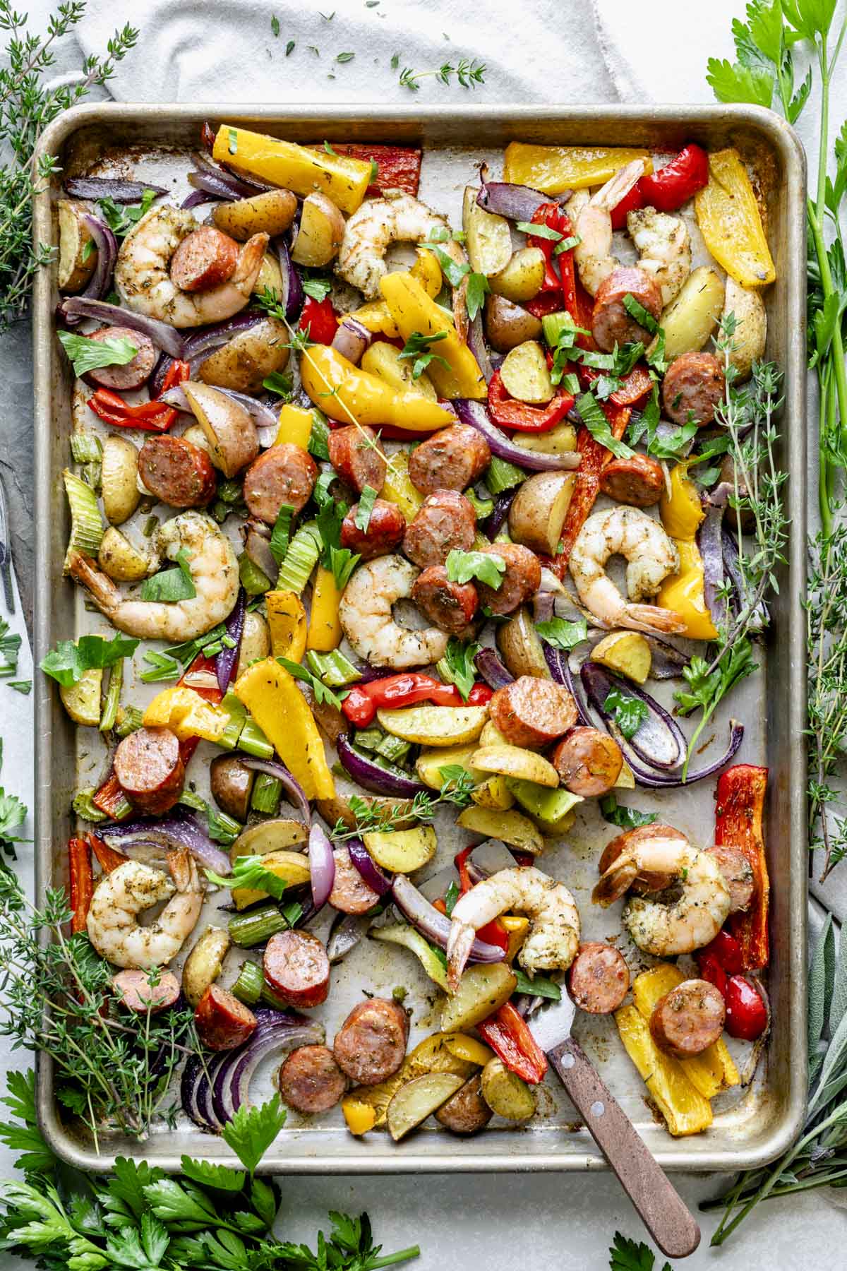 The sheet pan shrimp and sausage on the baking sheet from overhead with sprigs of fresh herbs all around it
