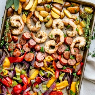 A sheet pan with potatoes, shrimp, sausage and peppers with sprigs of fresh herbs