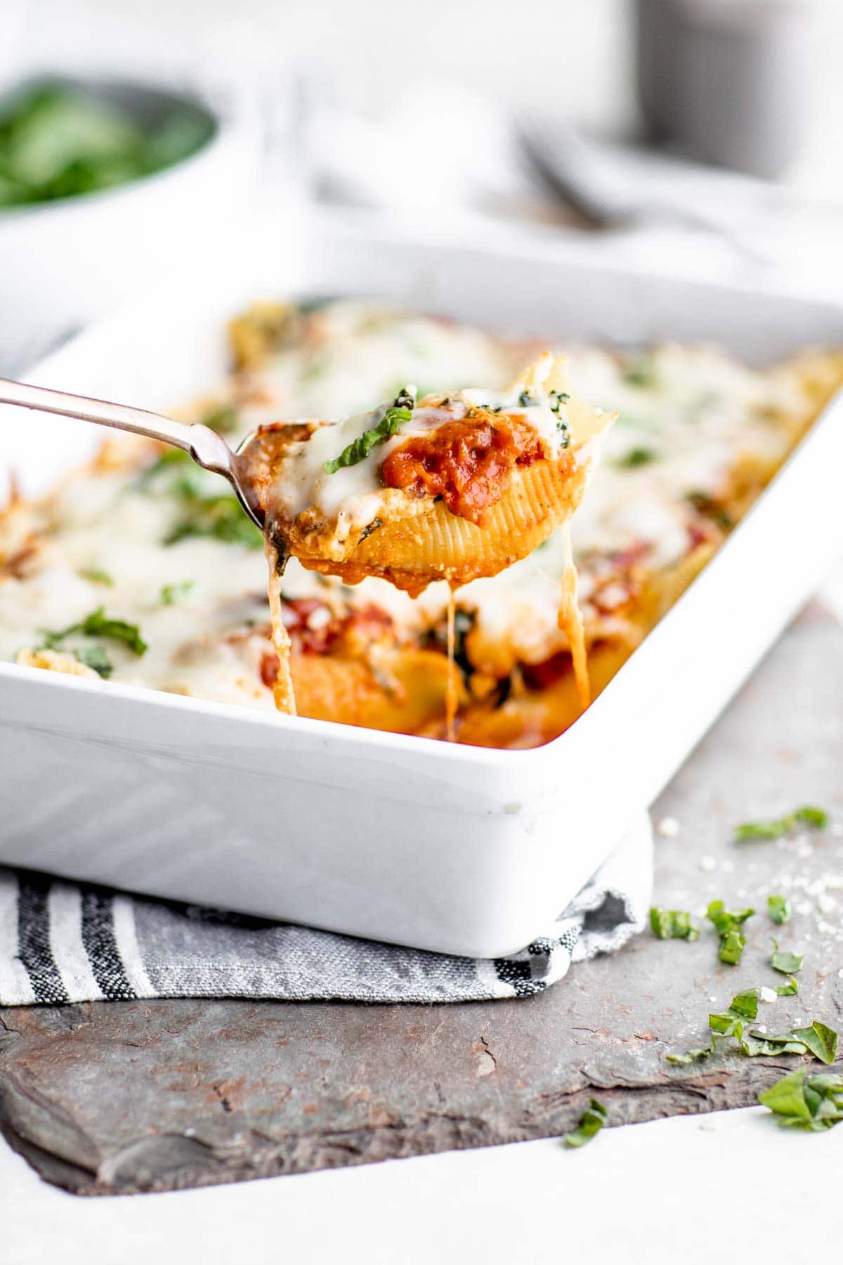 a single stuffed shell with spinach lifted out of the dish with cheese hanging from the spoon