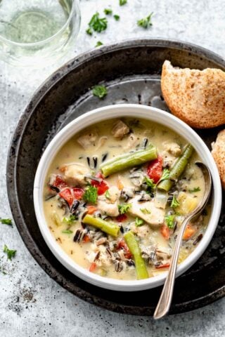 overhead of a bowl of wild rice soup on a black tin with a broken roll