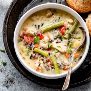 overhead of a bowl of wild rice soup on a black tin with a broken roll
