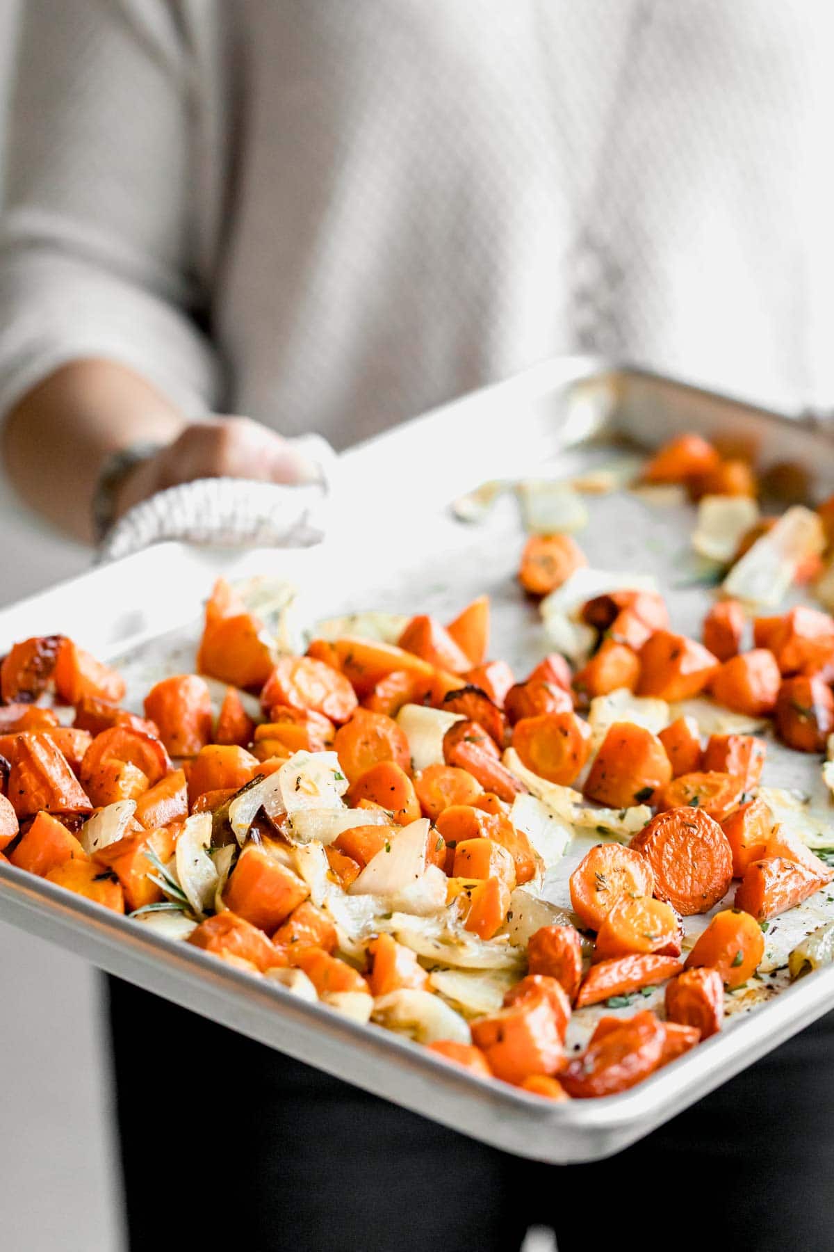 person holding sheet pan of roasted carrots and onions