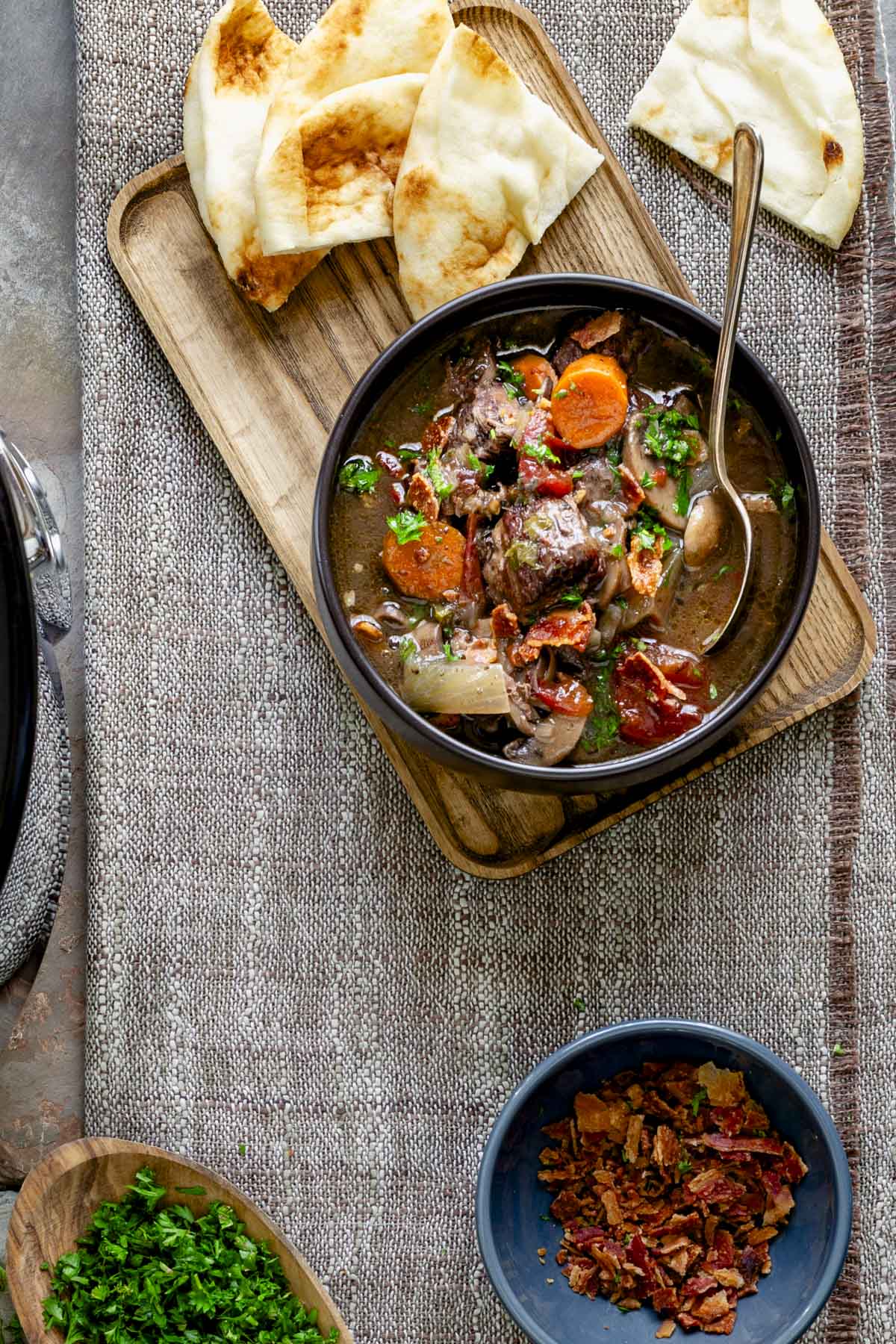 from overhead the beef burgundy in a black bowl on top of a wooden plate