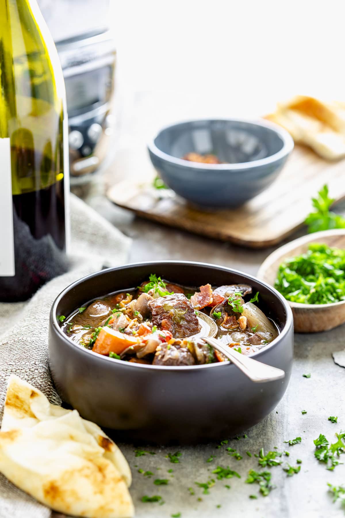 the stew from the side in a black bowl. The red wine and slow cooker are in the background