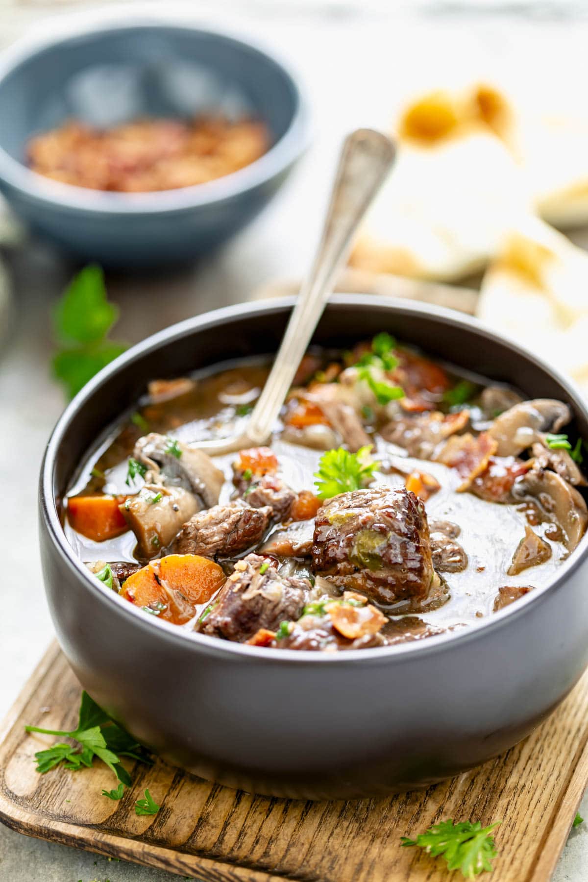 the beef stew in a black bowl with a spoon in it. There are chunks of beef, carrot and mushroom above the level of the liquid