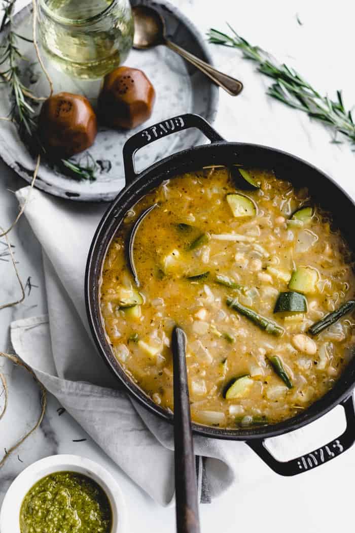 an overhead of a black soup pot with soupe au pistou in it and a bowl of pesto on the side