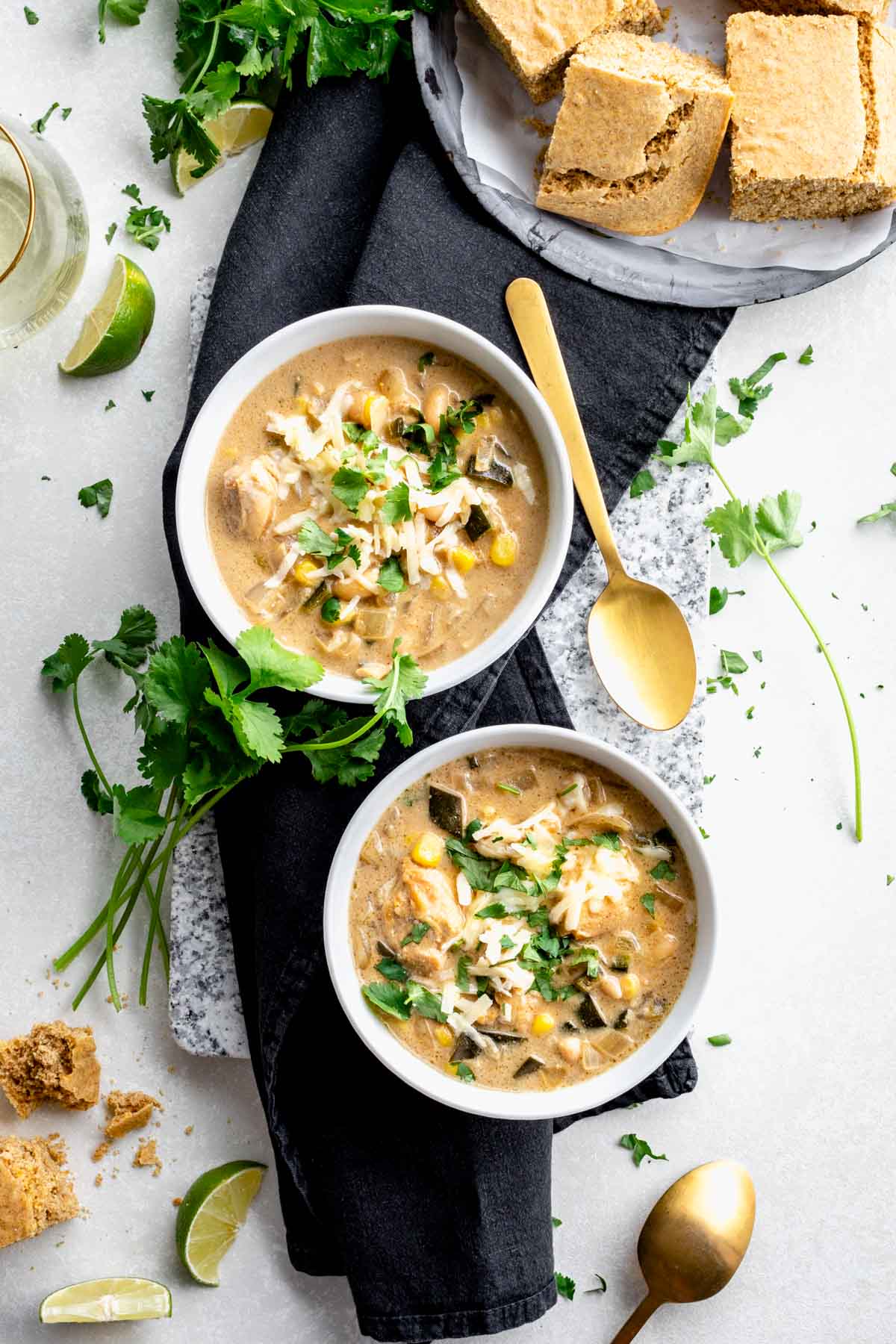 two bowls of chili with a gold spoon and tray of cornbread with black napkin