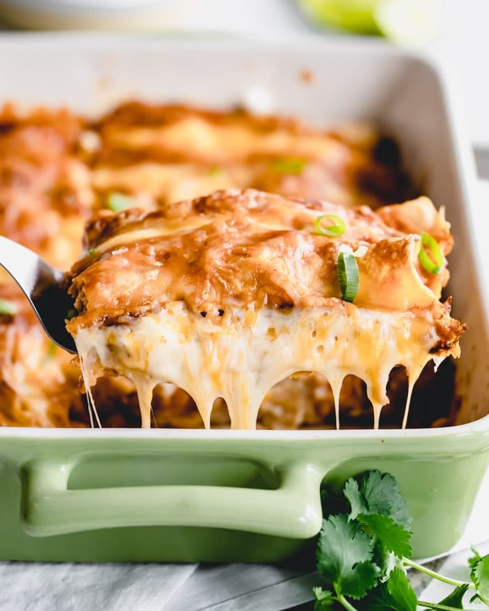 a close up side view of two enchiladas being lifted out of the casserole dish