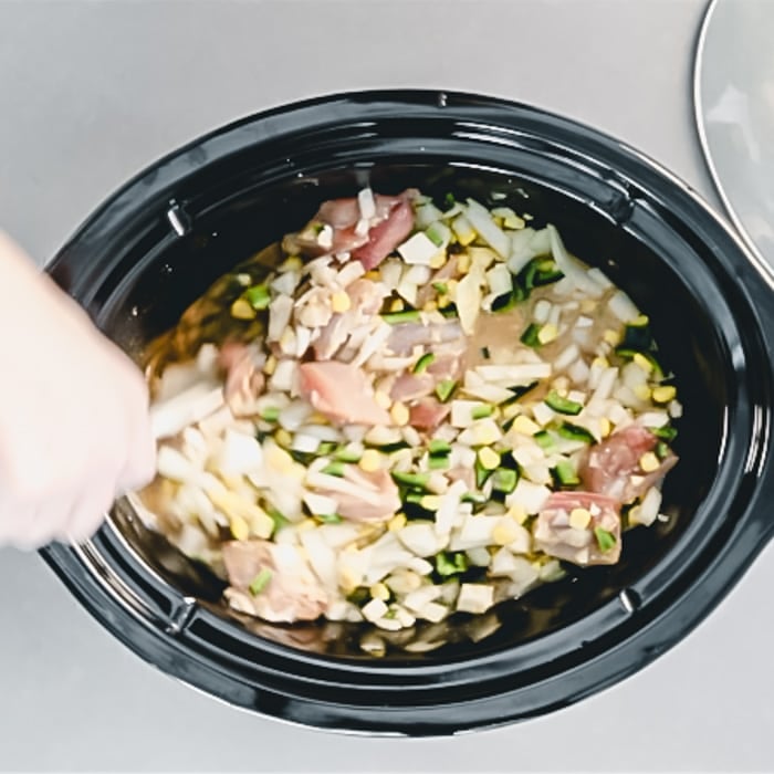 a hand stirring the chicken and vegetables together with the broth, cornmeal and spices
