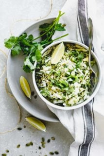 Coleslaw overhead in a single bowl with lime wedges and cilantro