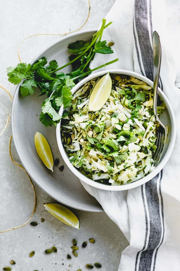 Coleslaw overhead in a single bowl with lime wedges and cilantro