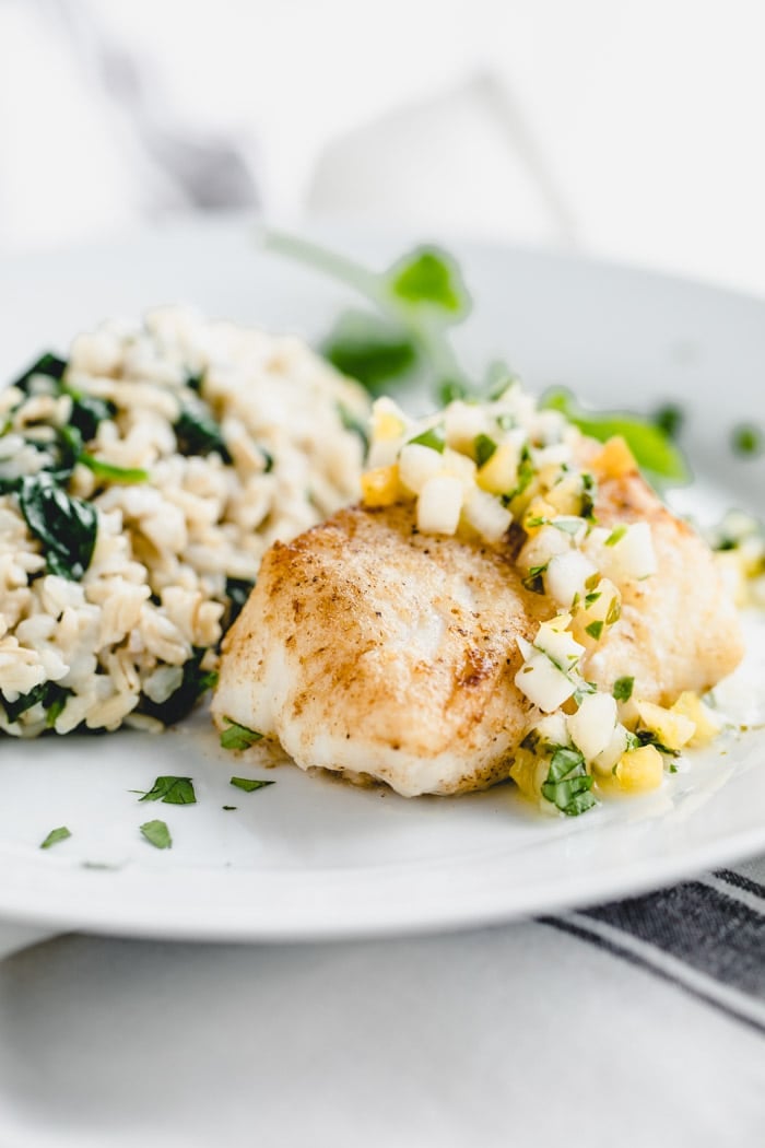 White plate with pan fried cod topped with pineapple salsa.