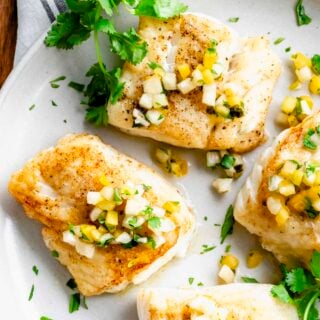 four pieces of fried fish on a white plate with cilantro